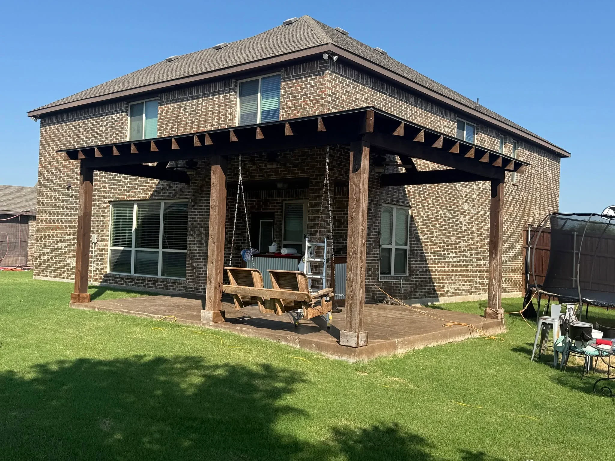 Wood pergola with lattice details, timber posts, and stained deck attached to brick home