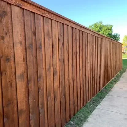 Vertical board wood privacy fence with medium-brown stain, concrete base installation