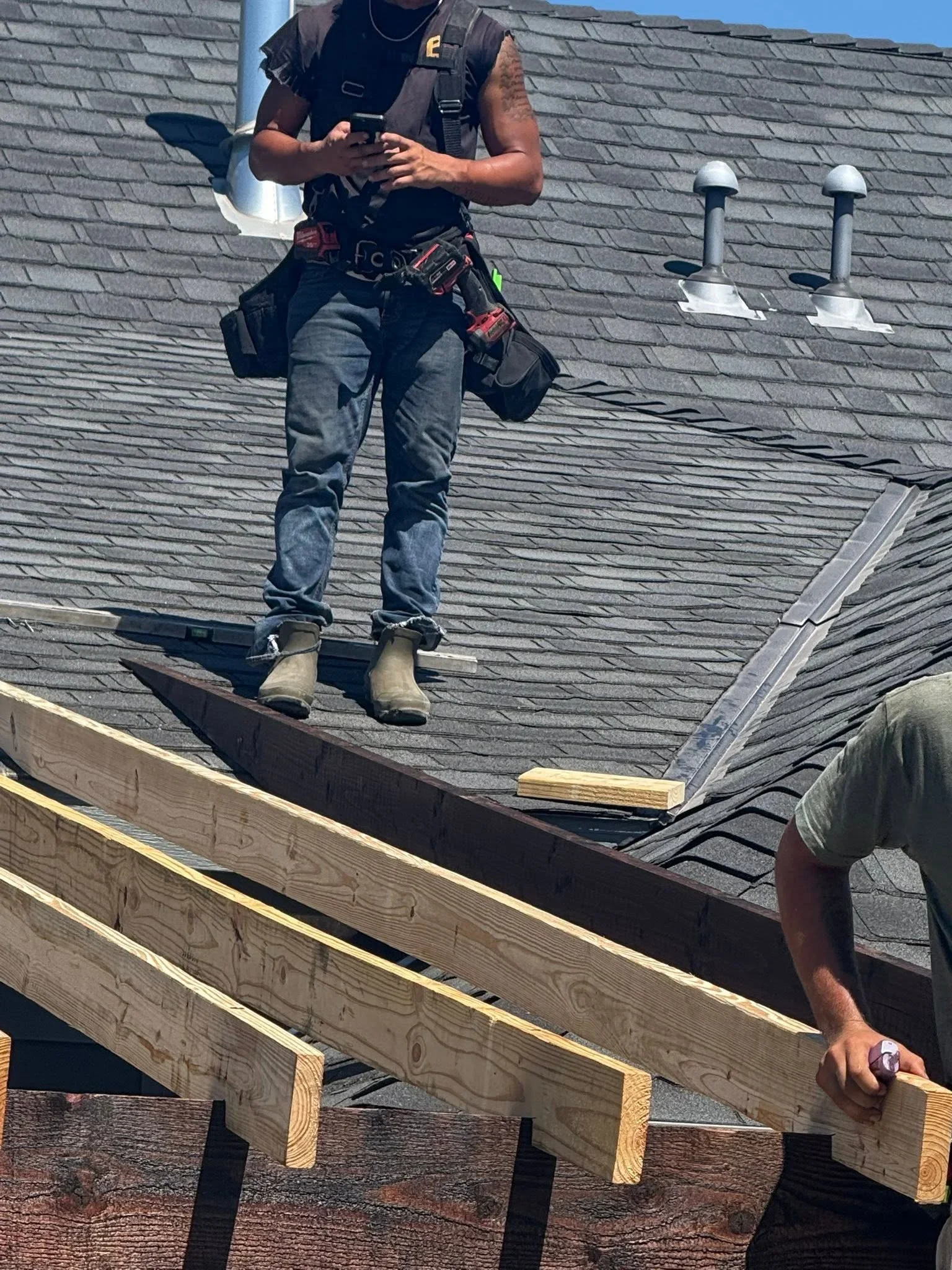Roofer inspecting asphalt shingle roof with pipe penetrations and metal flashing