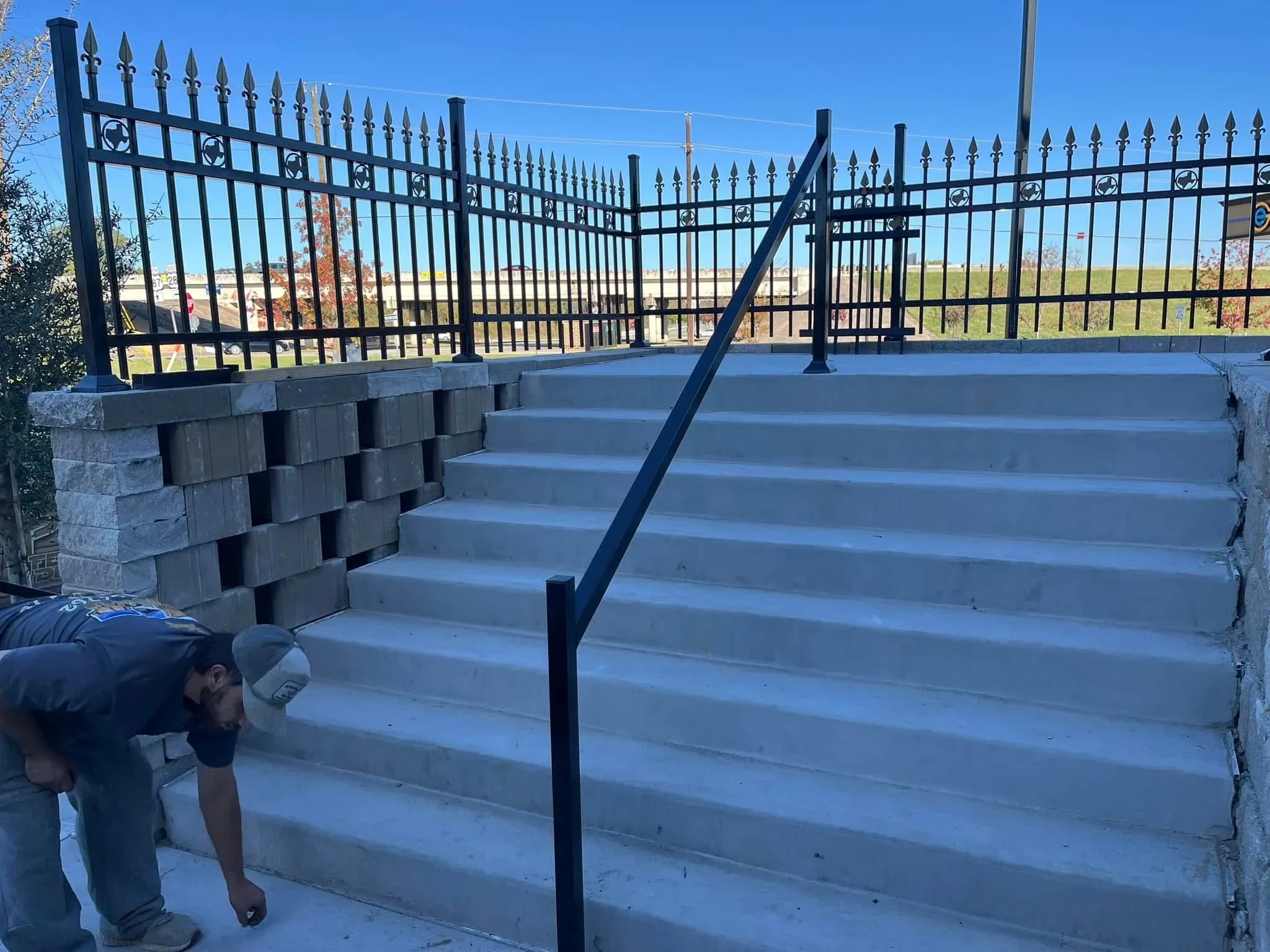 Black ornamental iron fence with spear pickets, concrete base, and steel handrail on stepped entrance