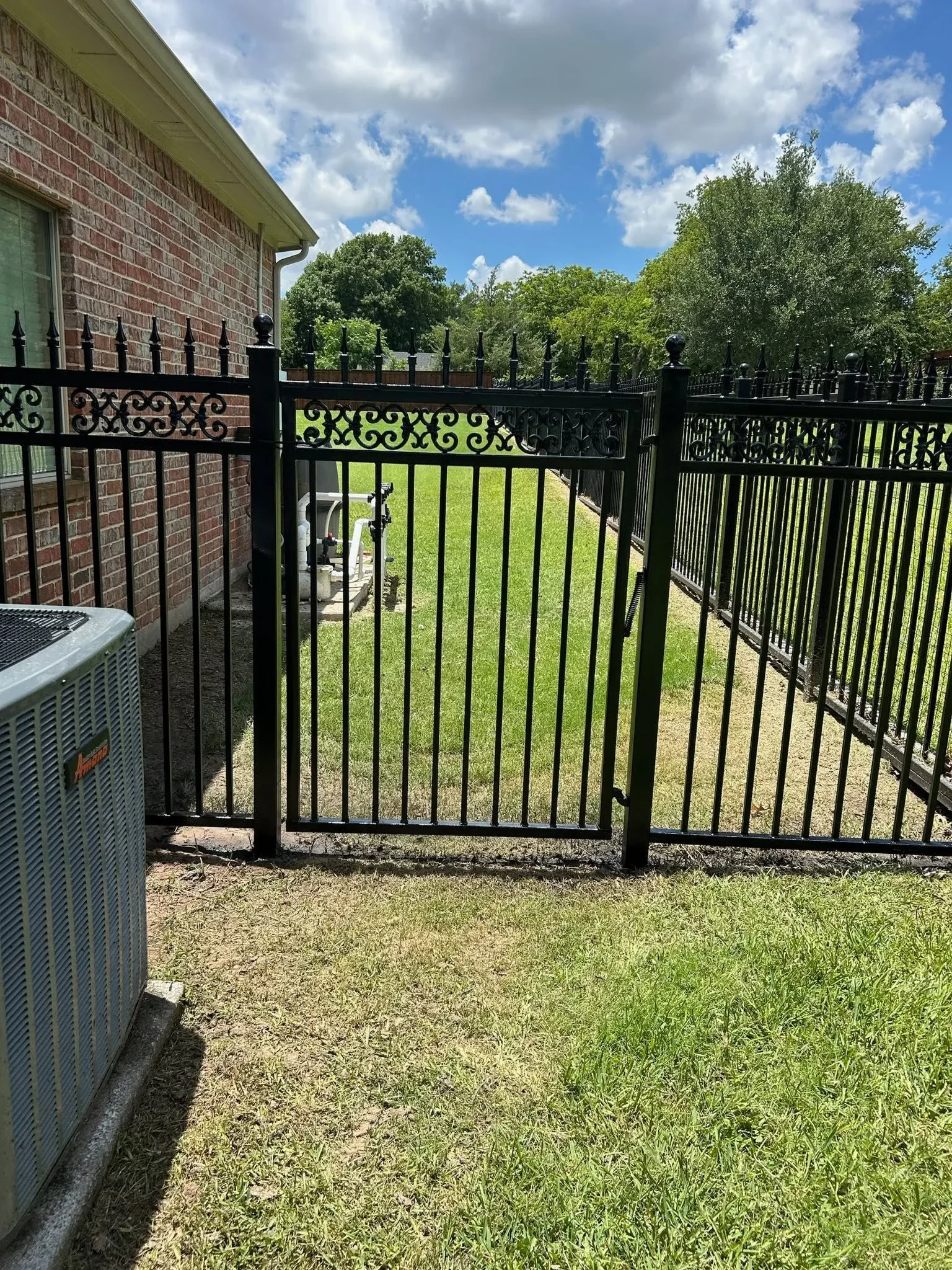 Black ornamental iron fence with scrollwork design and matching gate installed at residential property