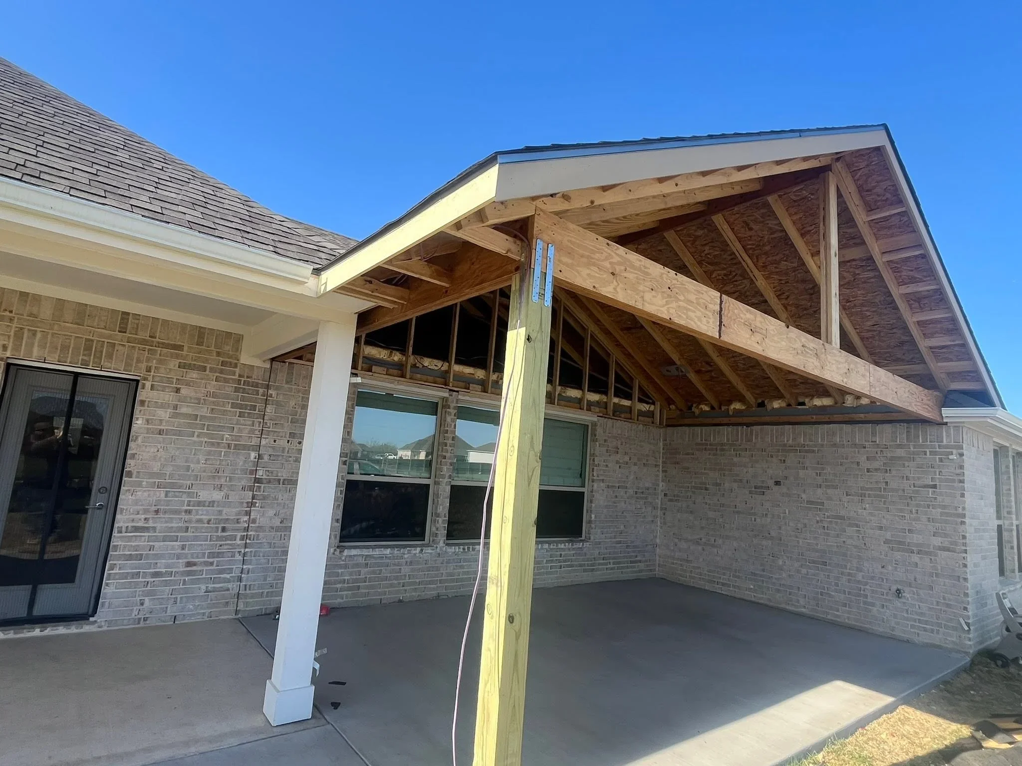Covered patio with exposed wood beams, trusses, and large windows attached to brick home