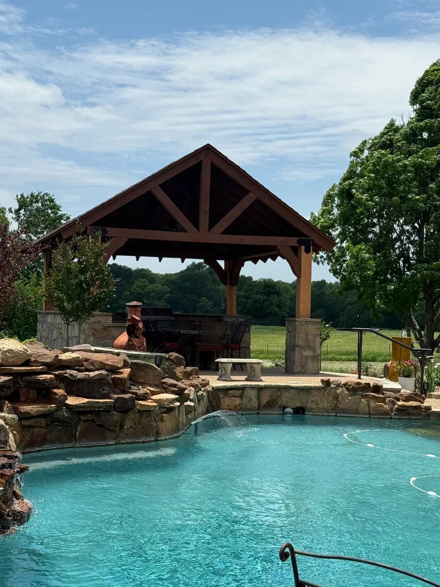 Timber pavilion with gabled roof over pool with stone waterfall and masonry pillars