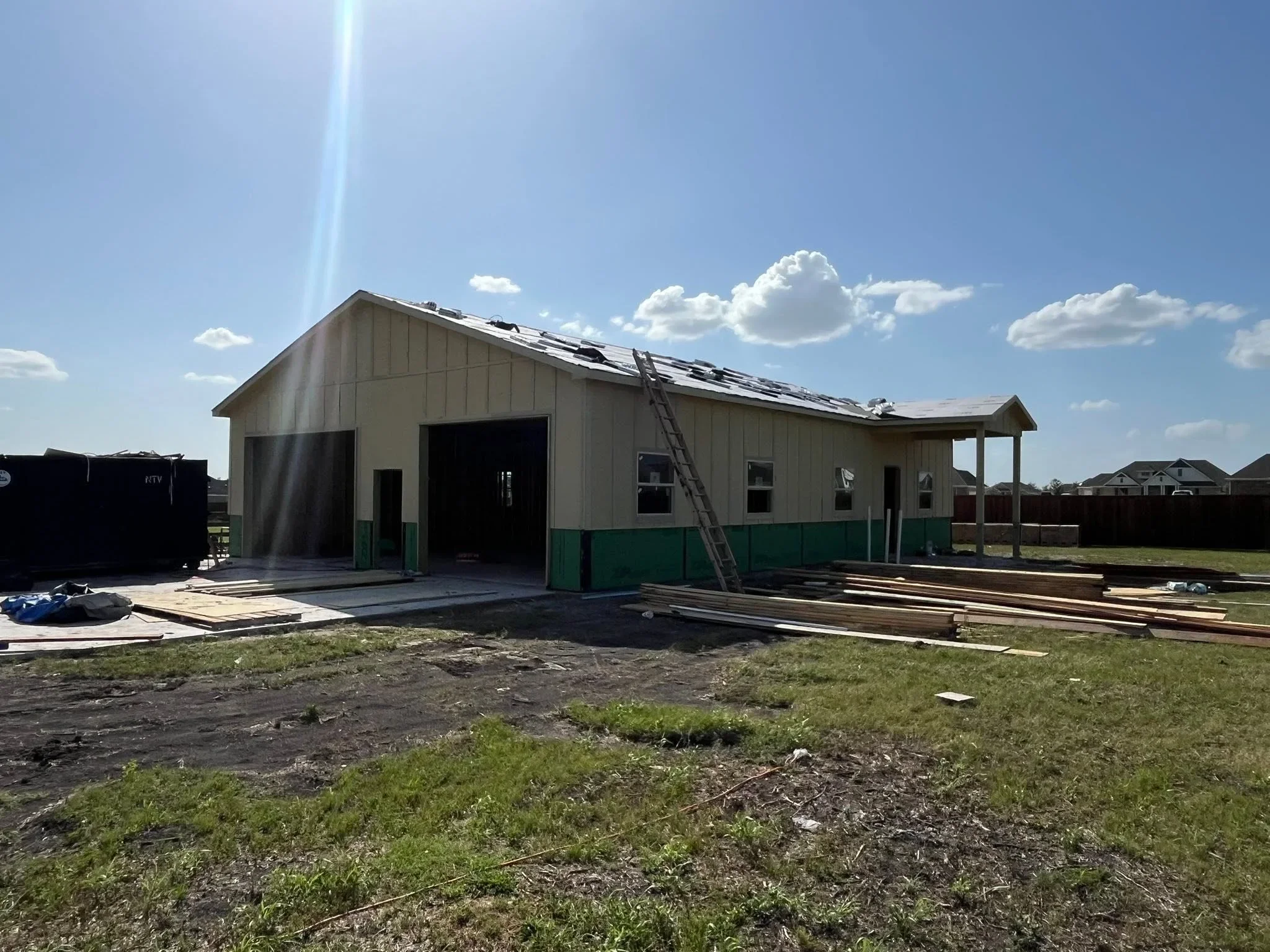 Metal building with tan siding, green trim, and covered porch during construction phase
