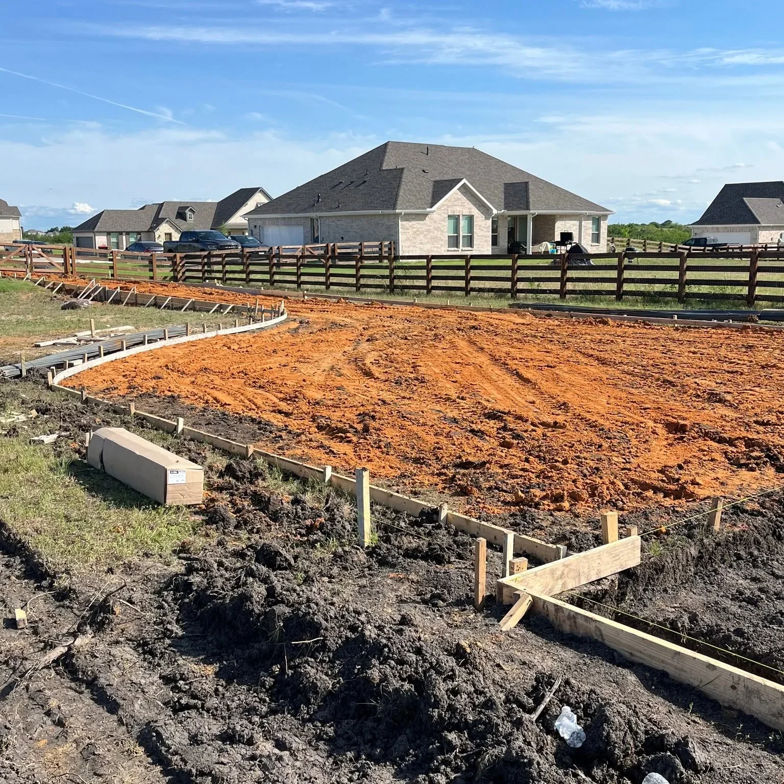 Split-rail wooden fence installation with concrete footers and graded red clay site preparation on ranch property