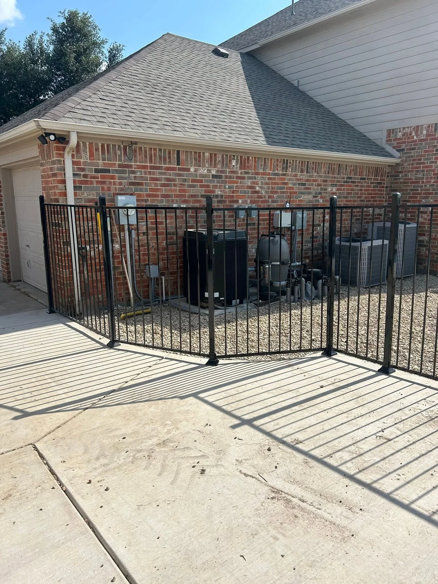 Black aluminum fence enclosure around HVAC units on composite deck with brick home backdrop