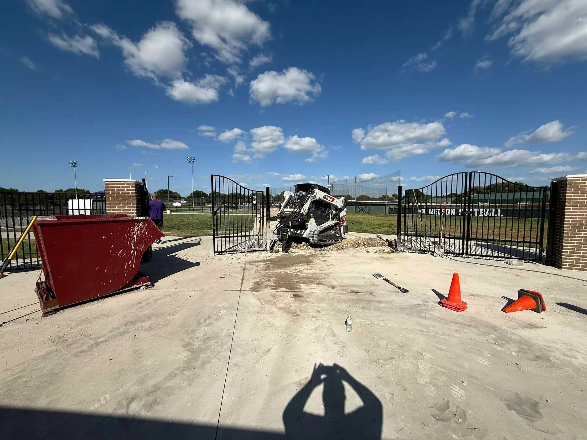 Black ornamental steel fence with arched gates and brick pillars at sports facility