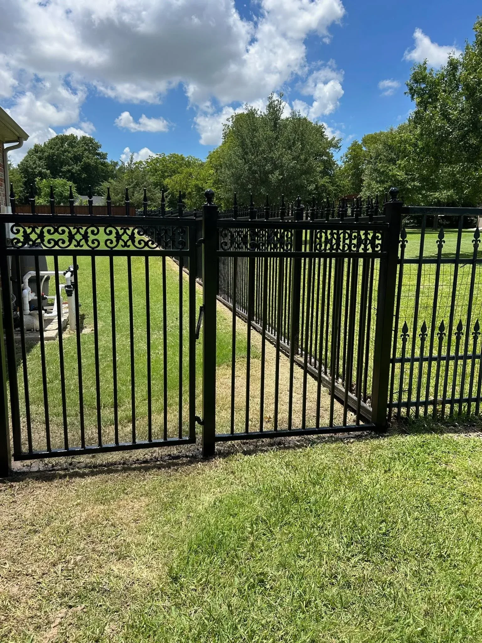 Black ornamental iron driveway gates with decorative scrollwork and vertical pickets