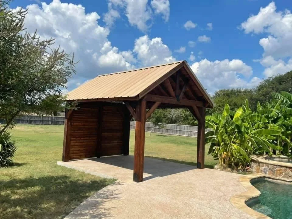 Wooden carport with metal roof, timber frame, and concrete pad in rural setting