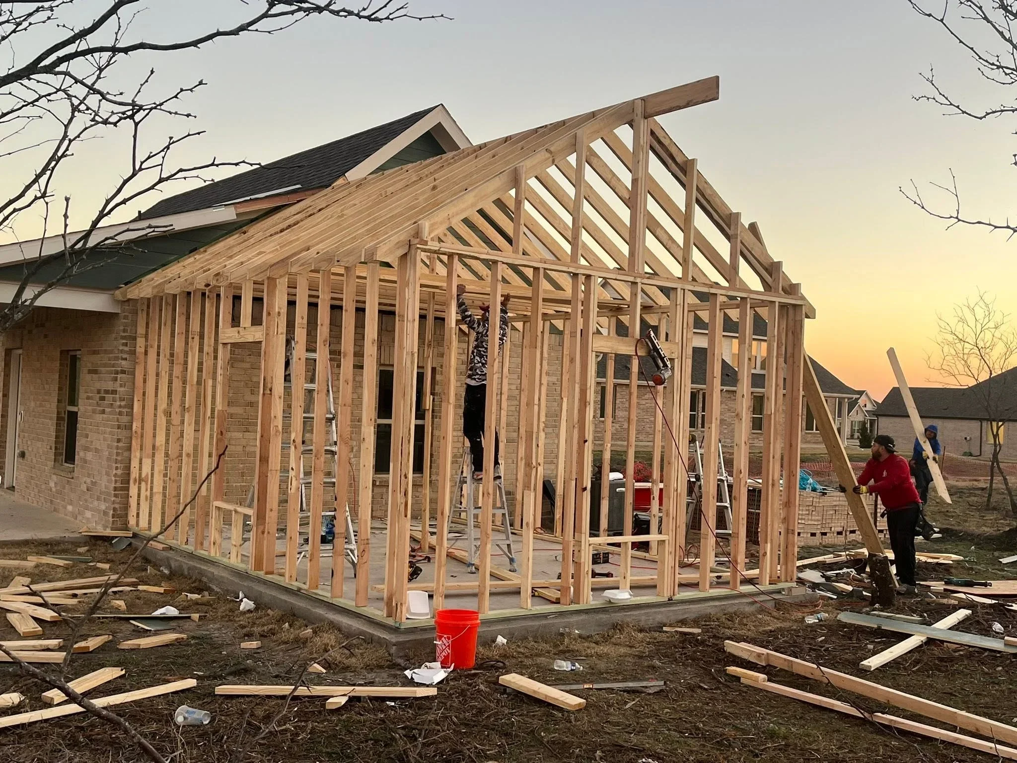 Wood-framed residential addition with dimensional lumber studs, rafters, and gable roof trusses during construction phase