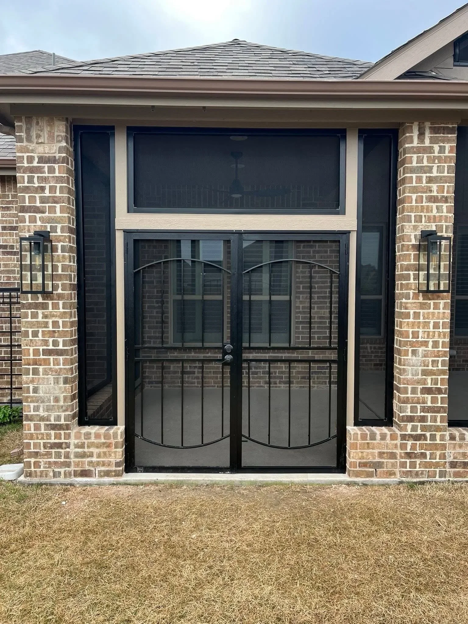 Black metal double gates with arch design and screen panels between brick pillars