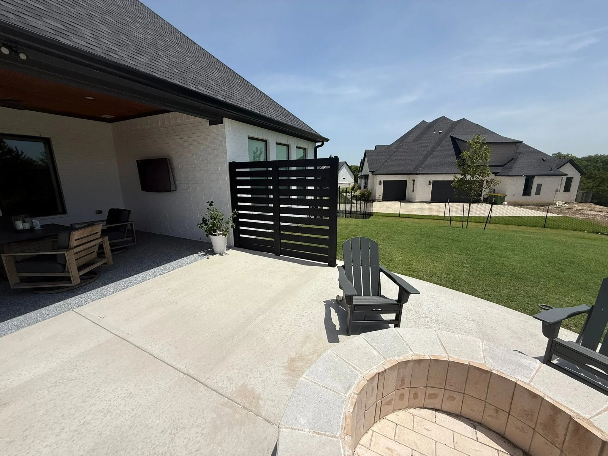Black horizontal slat privacy gate with modern home, concrete patio, and manicured lawn