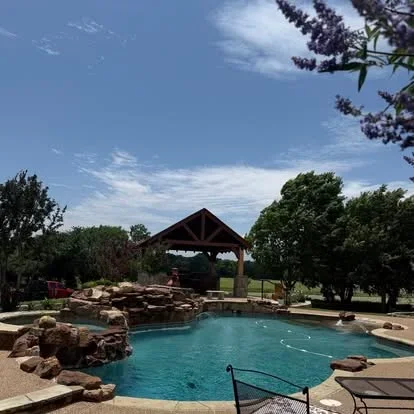 Timber pavilion over turquoise pool with natural stone boulders and mature landscaping