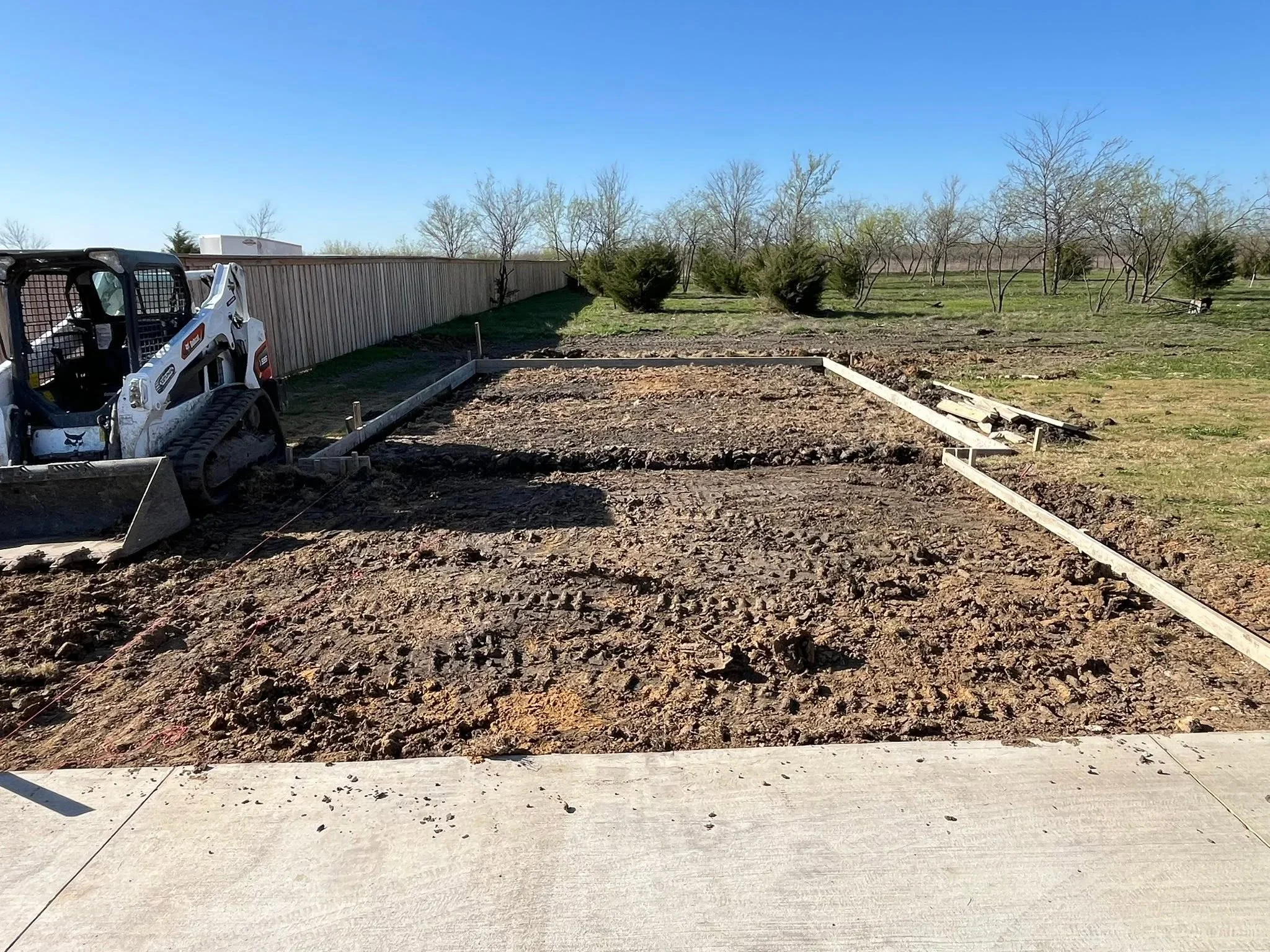 Skid steer loader grading lot with vinyl fence framing and white posts installed