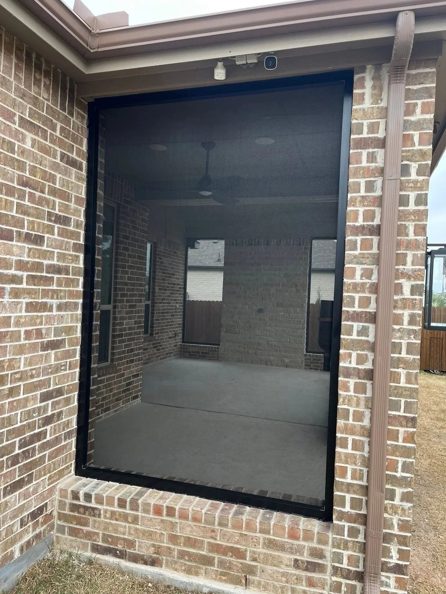Black retractable screen door mounted in brick patio opening with metal frame