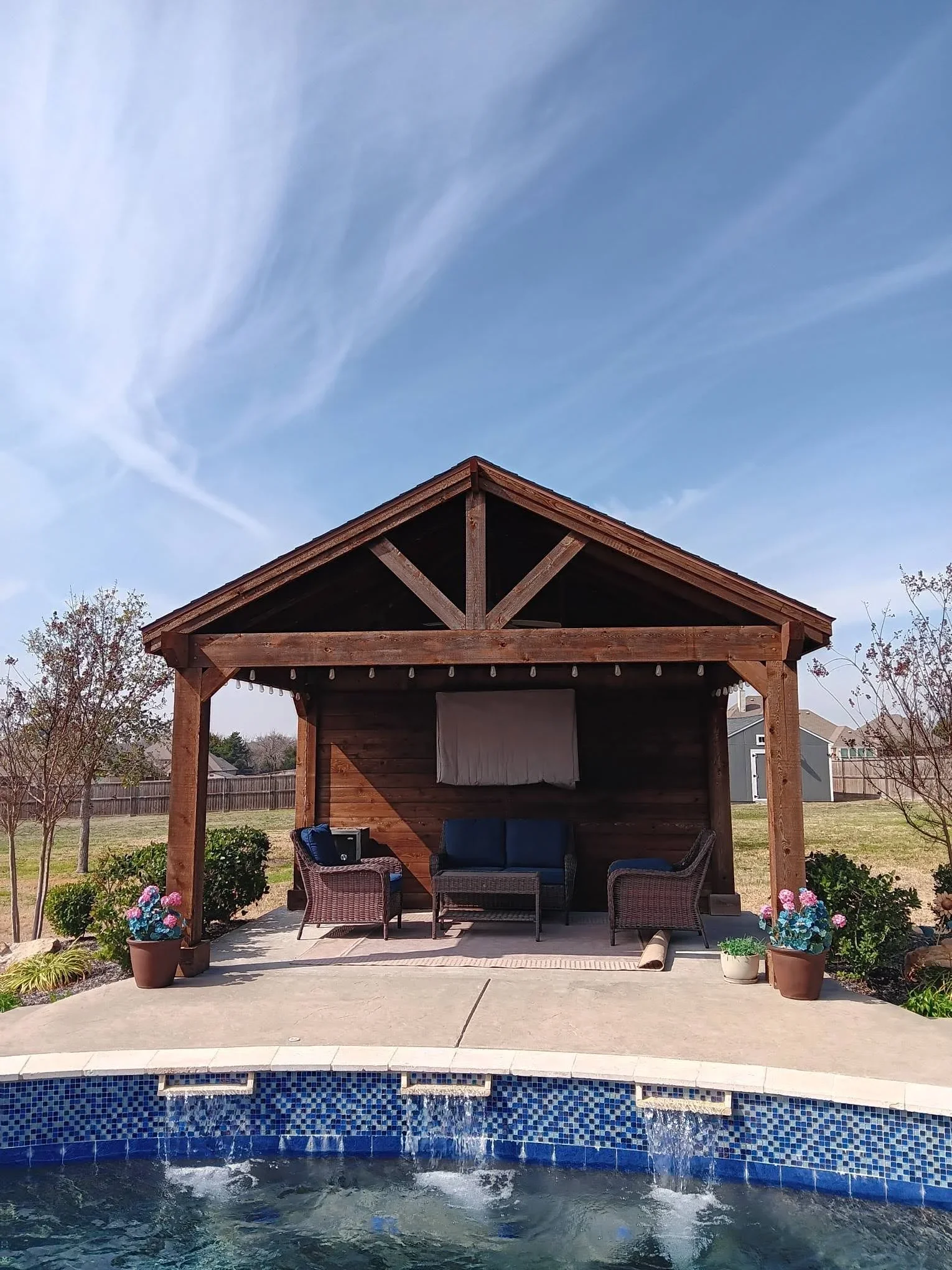 Timber pavilion with X-braced gable over concrete patio beside pool with blue tile waterline