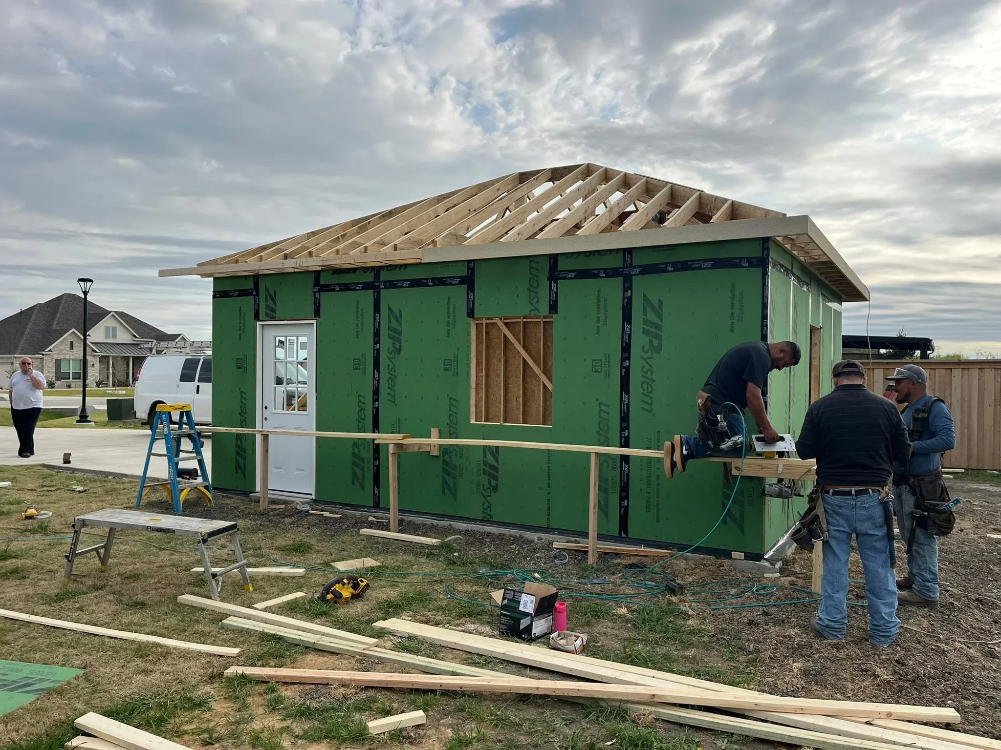 New home framing with roof trusses, green house wrap sheathing, and entry door installation in progress
