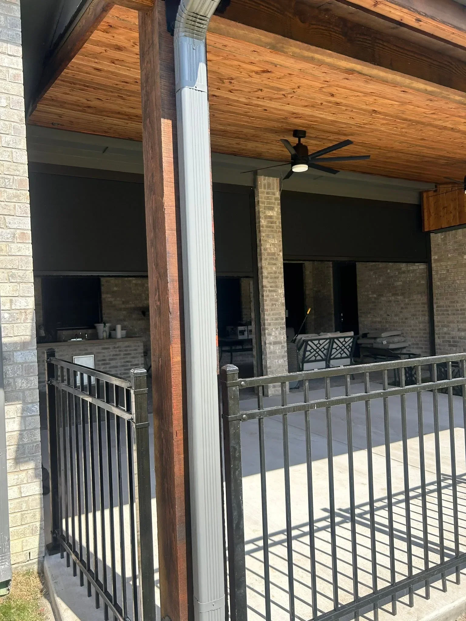 Metal railing with vertical balusters on covered patio with wood ceiling and brick columns