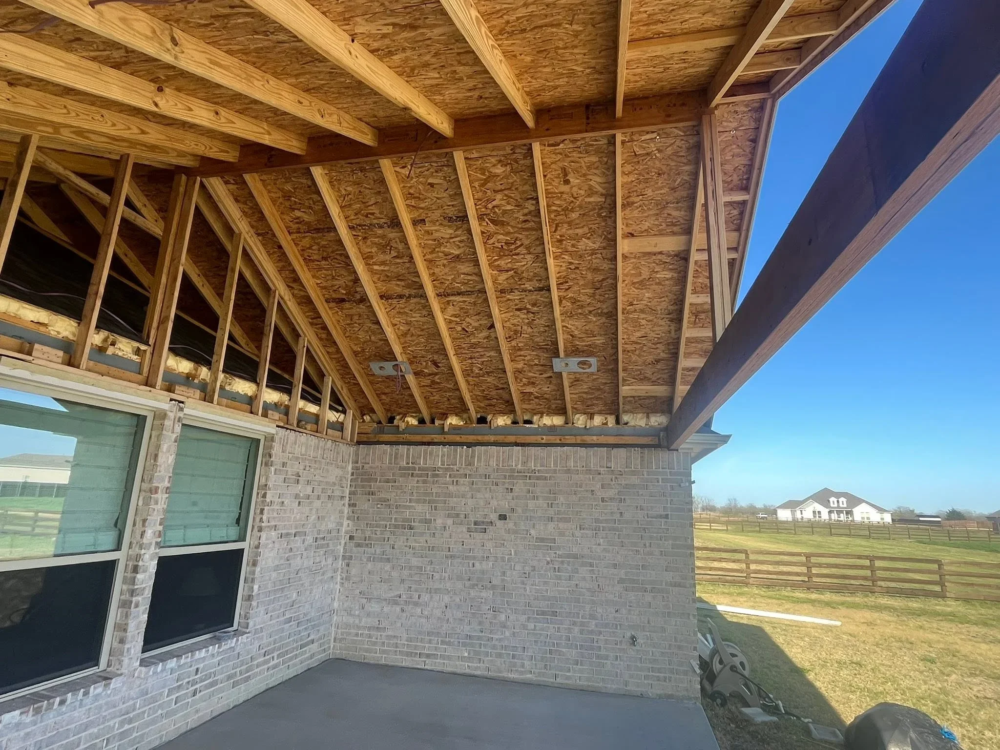Covered patio with exposed wood beam framing, OSB sheathing, brick walls, and sliding glass doors