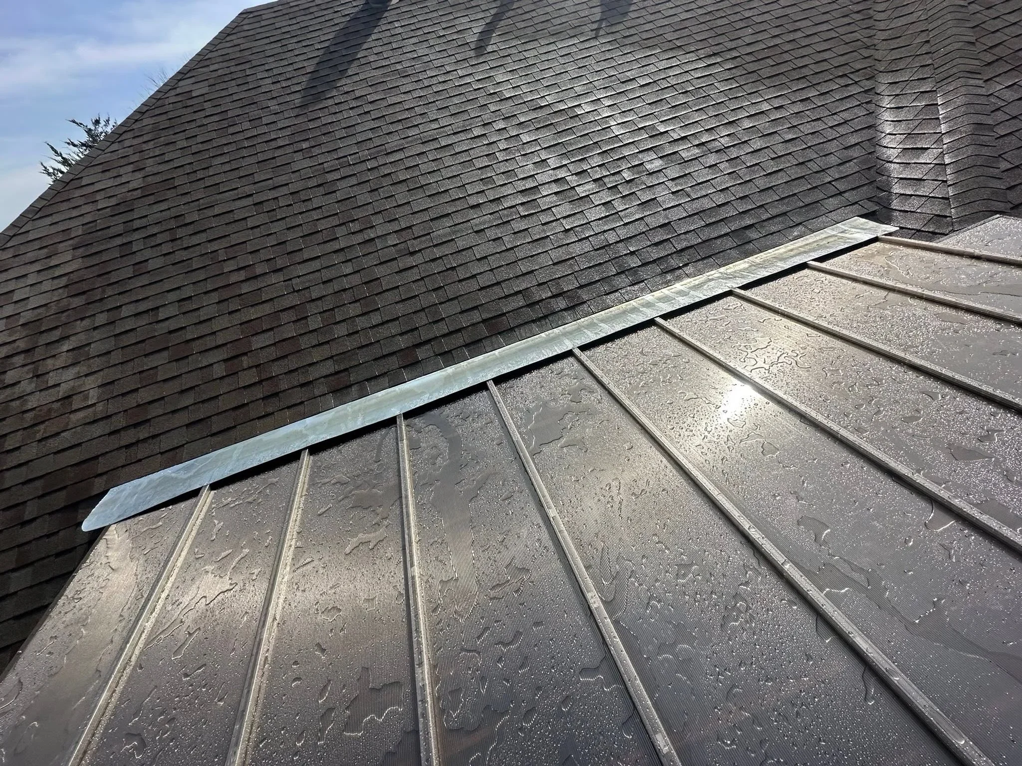 Standing seam metal roof with charcoal panels and aluminum flashing installed over shingle roof