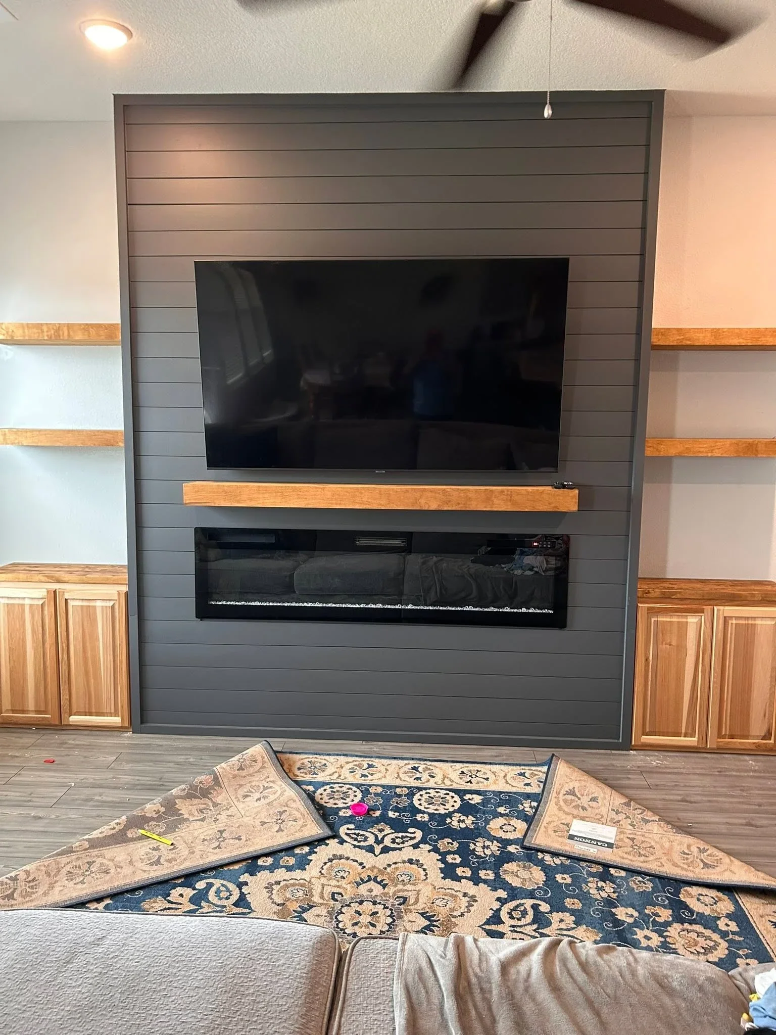 Gray shiplap entertainment wall with mounted TV, electric fireplace, wood shelves and cabinetry