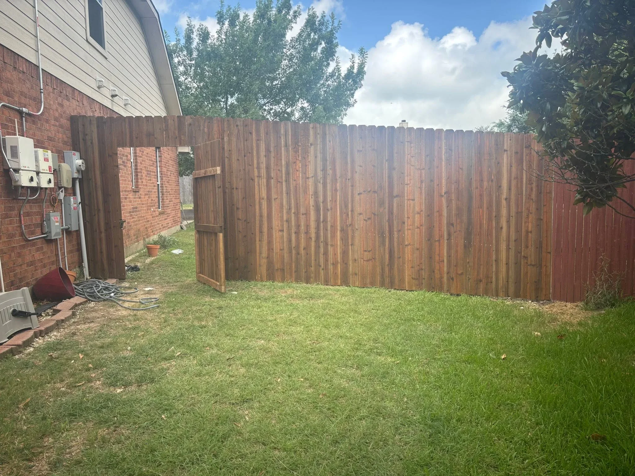 Newly installed wood privacy fence with vertical boards and gate, stained brown finish