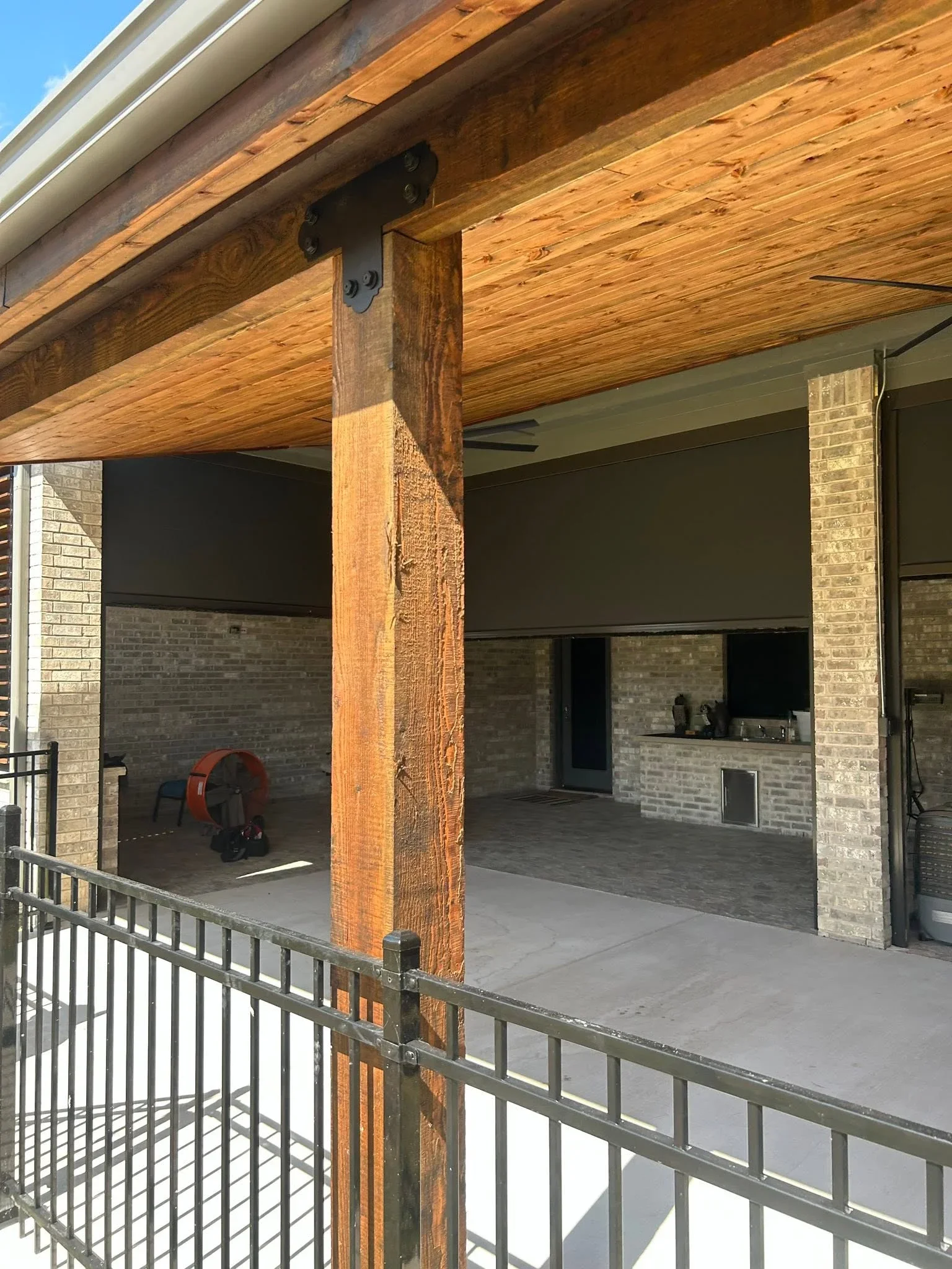 Covered patio with timber beams, brick columns, metal railing, and concrete floor