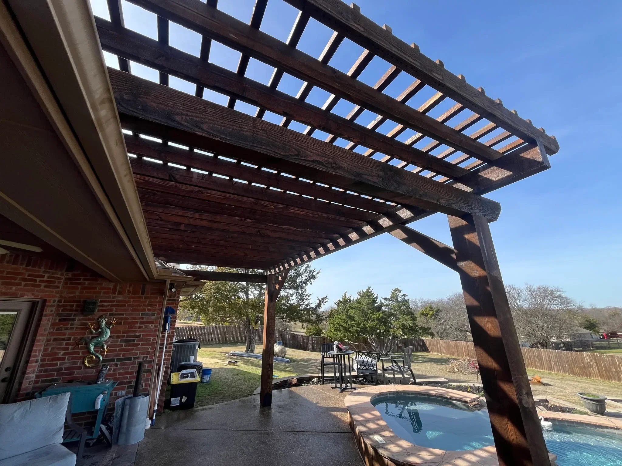 Dark wood pergola with lattice slats over concrete patio and pool area