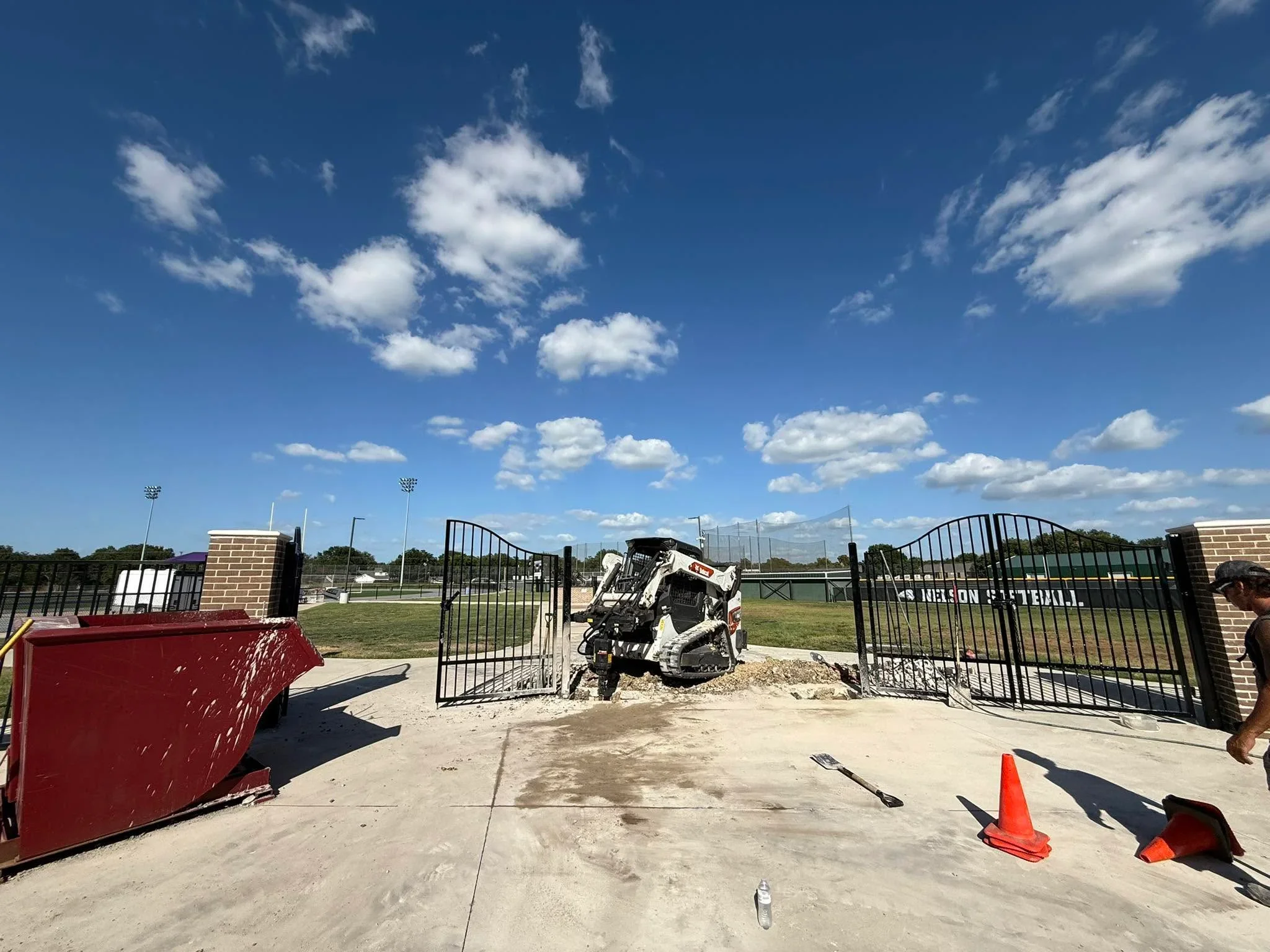 Black aluminum arched driveway gates at sports complex entrance with concrete pad and brick pillars