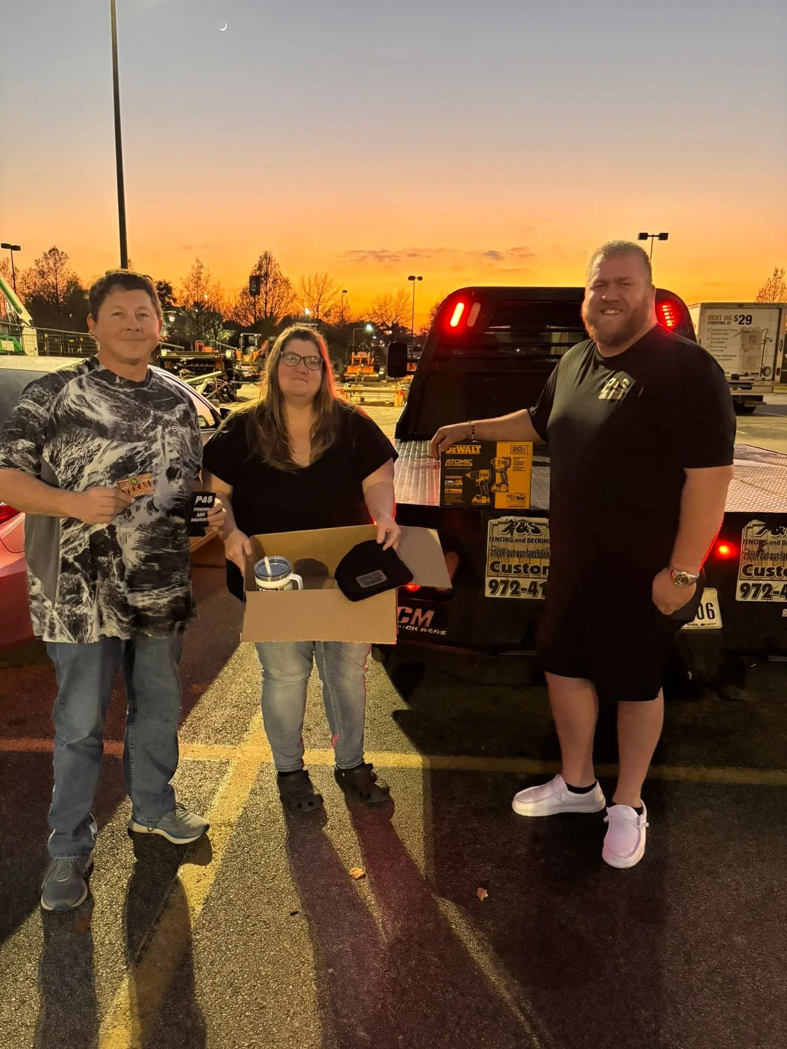 Three people holding DeWalt tool kit box at outdoor customer appreciation event
