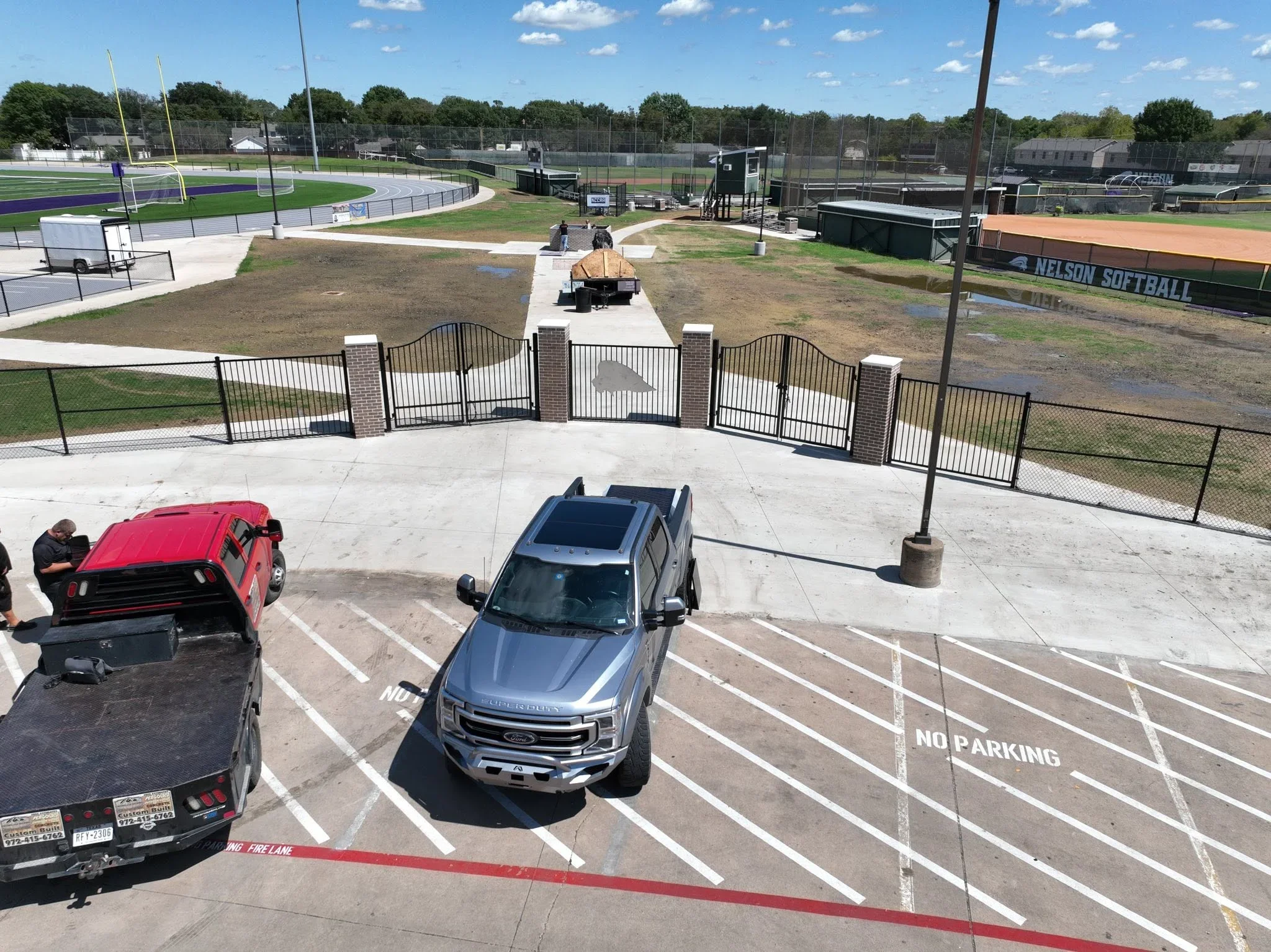 Black metal ornamental gate with brick pillars at sports complex entrance with concrete apron