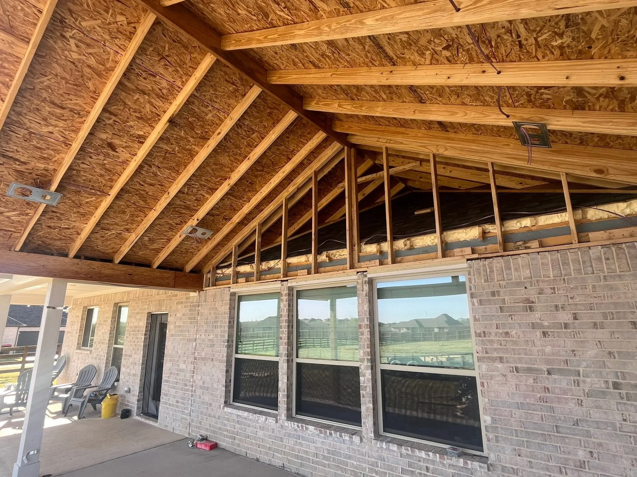 Covered patio with exposed wood beams, OSB sheathing, brick walls, and sliding glass doors