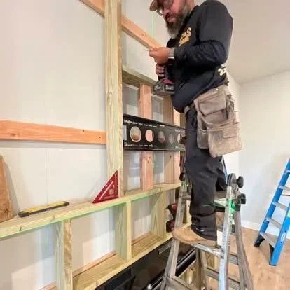 Carpenter installing wooden frame and shelving units on interior wall with level and tools