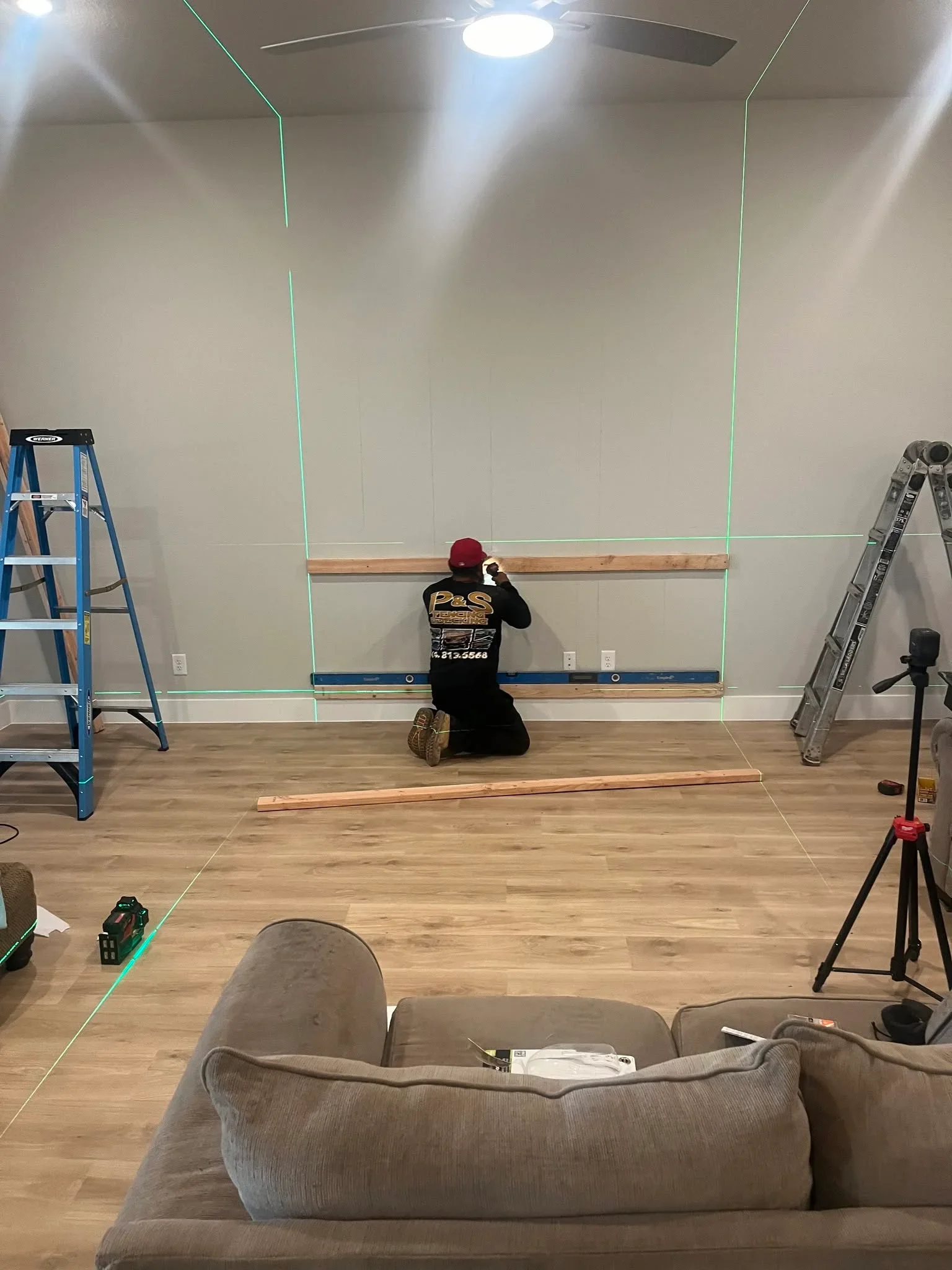 Drywall installation with green laser layout lines, wood trim rail, and finished ceiling with fan