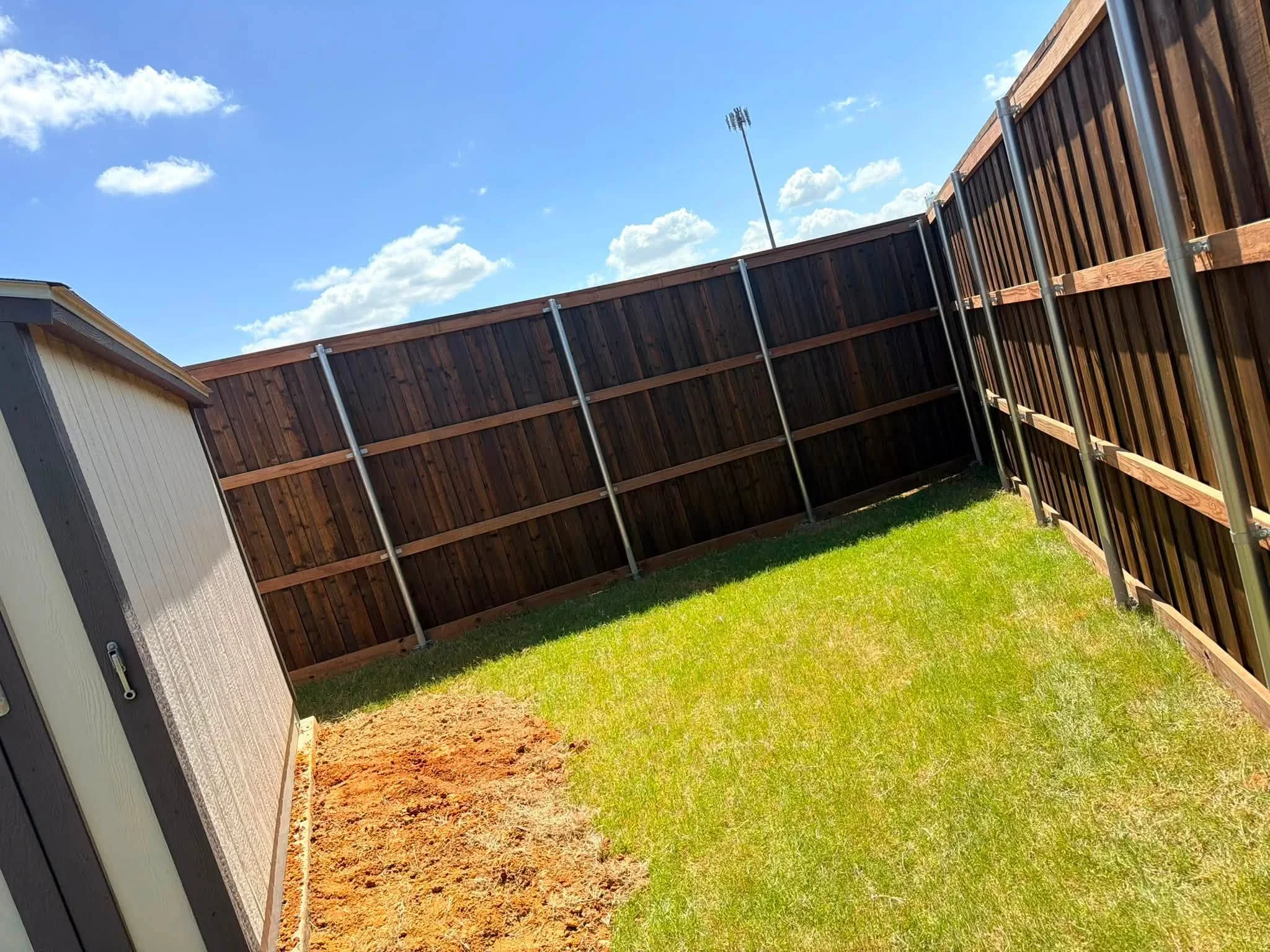 Stained wood fence with metal posts and horizontal bracing in residential yard
