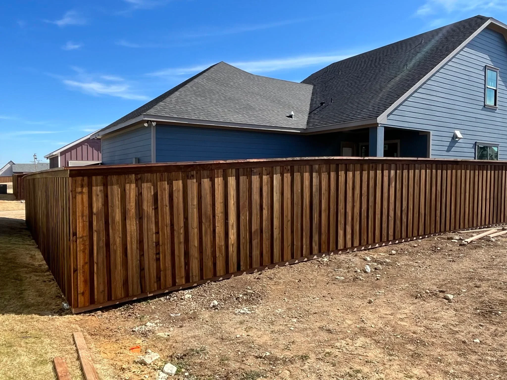 Vertical wood privacy fence with brown stain, newly installed along residential property line