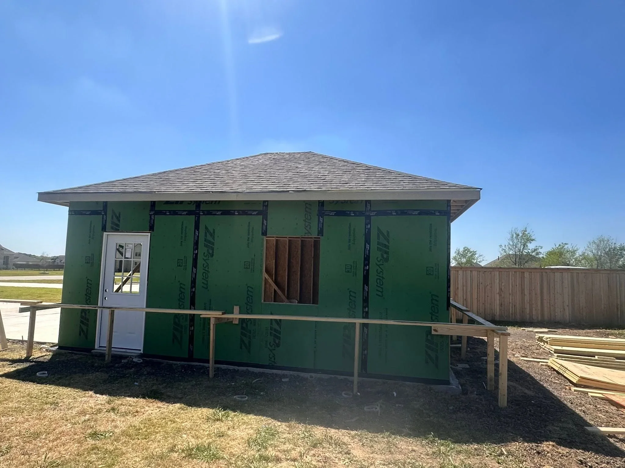 Home framing with green house wrap, asphalt shingle roof, and wooden porch structure