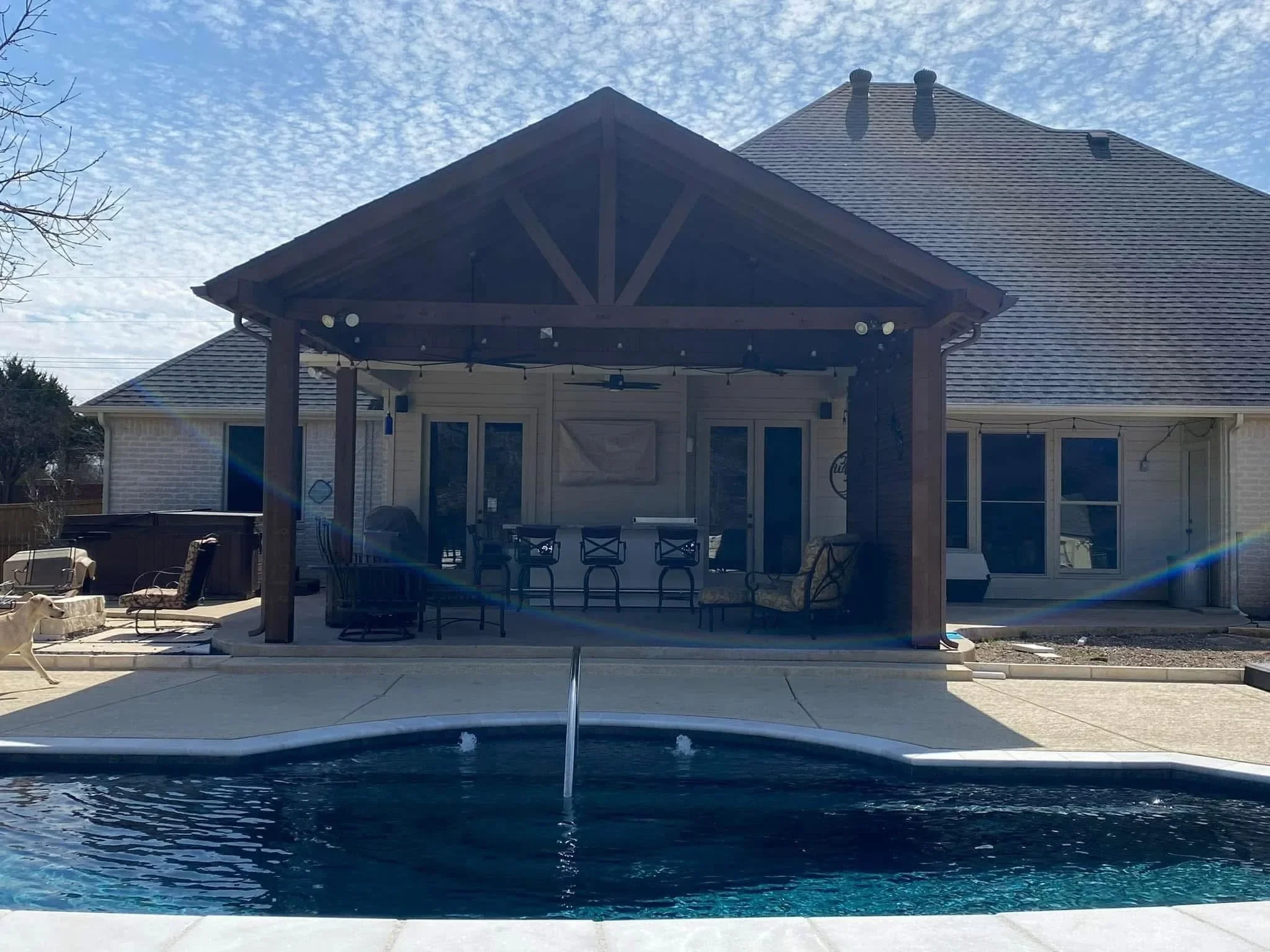 Dark wood pergola with cross-bracing over concrete patio beside in-ground pool