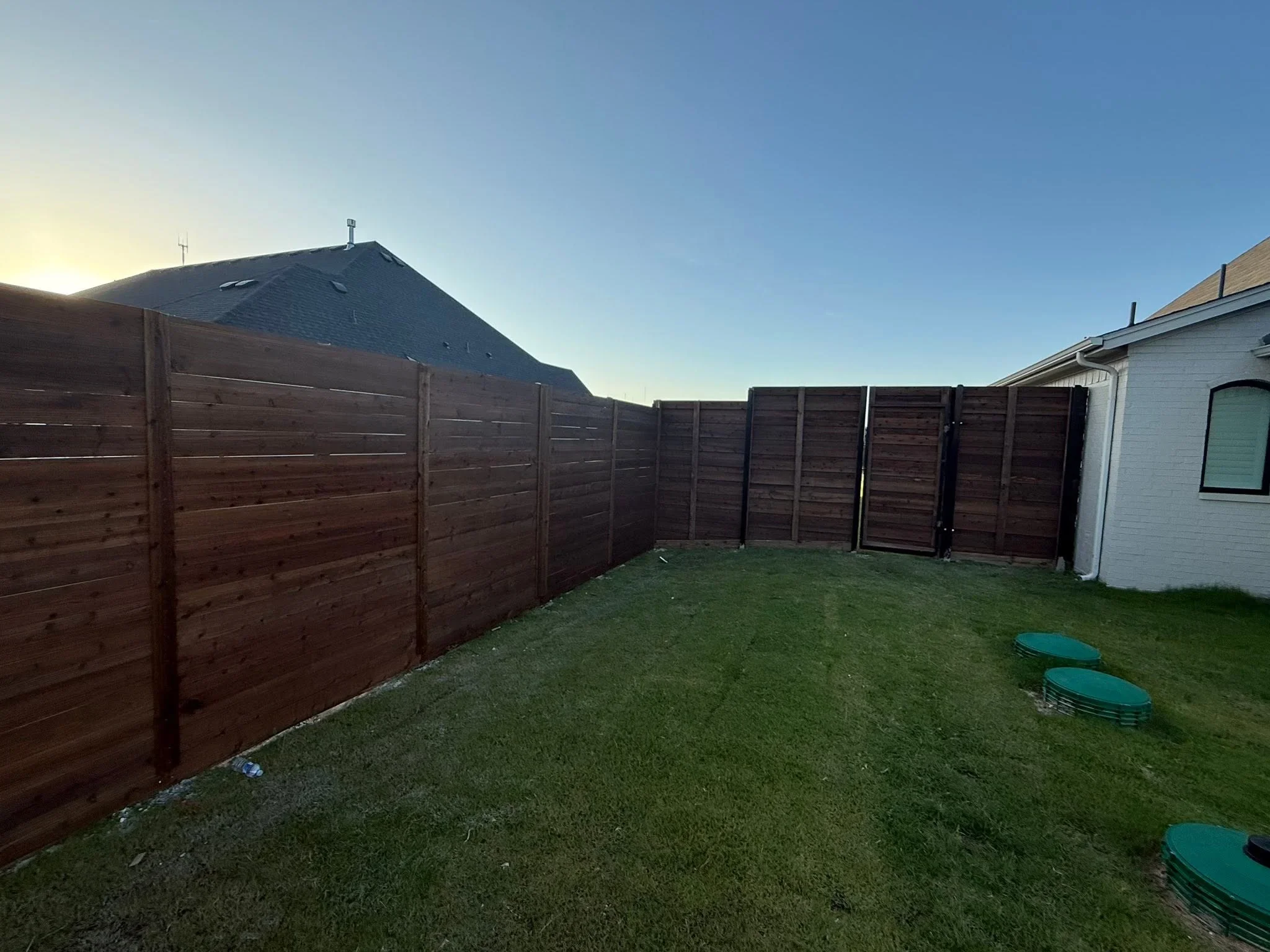Dark stained horizontal wood privacy fence panels installed around residential backyard with green lawn