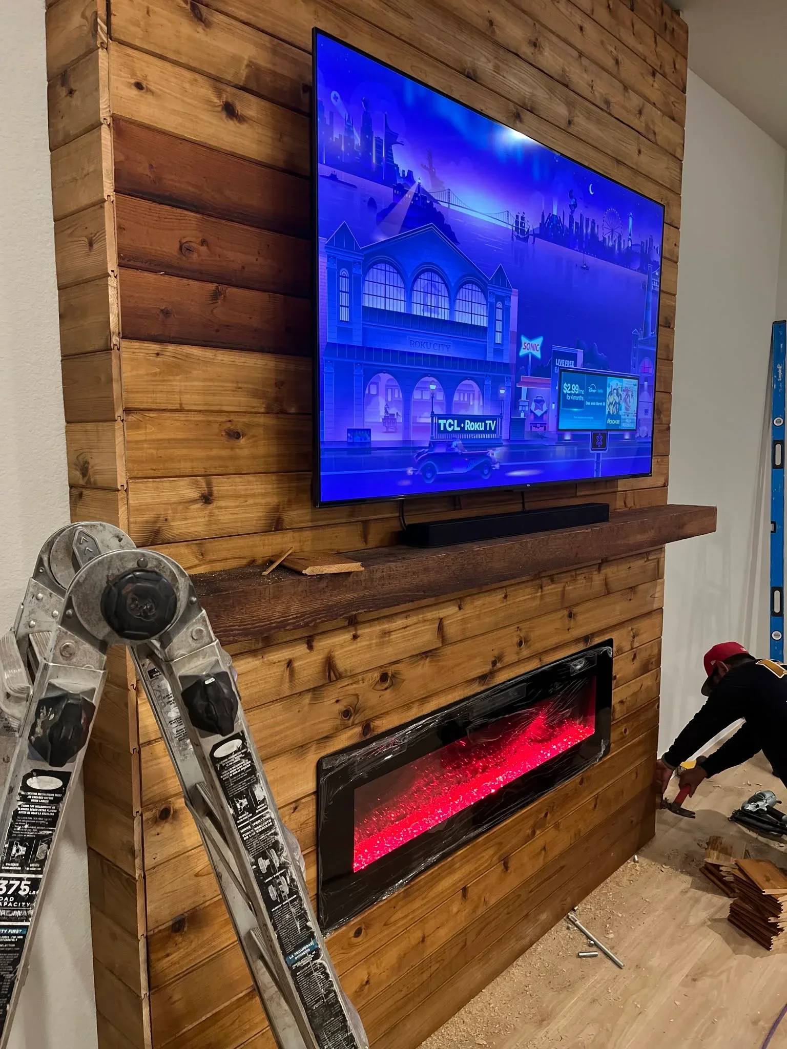 Rustic wood shiplap wall with mounted TV, electric fireplace, and media shelving