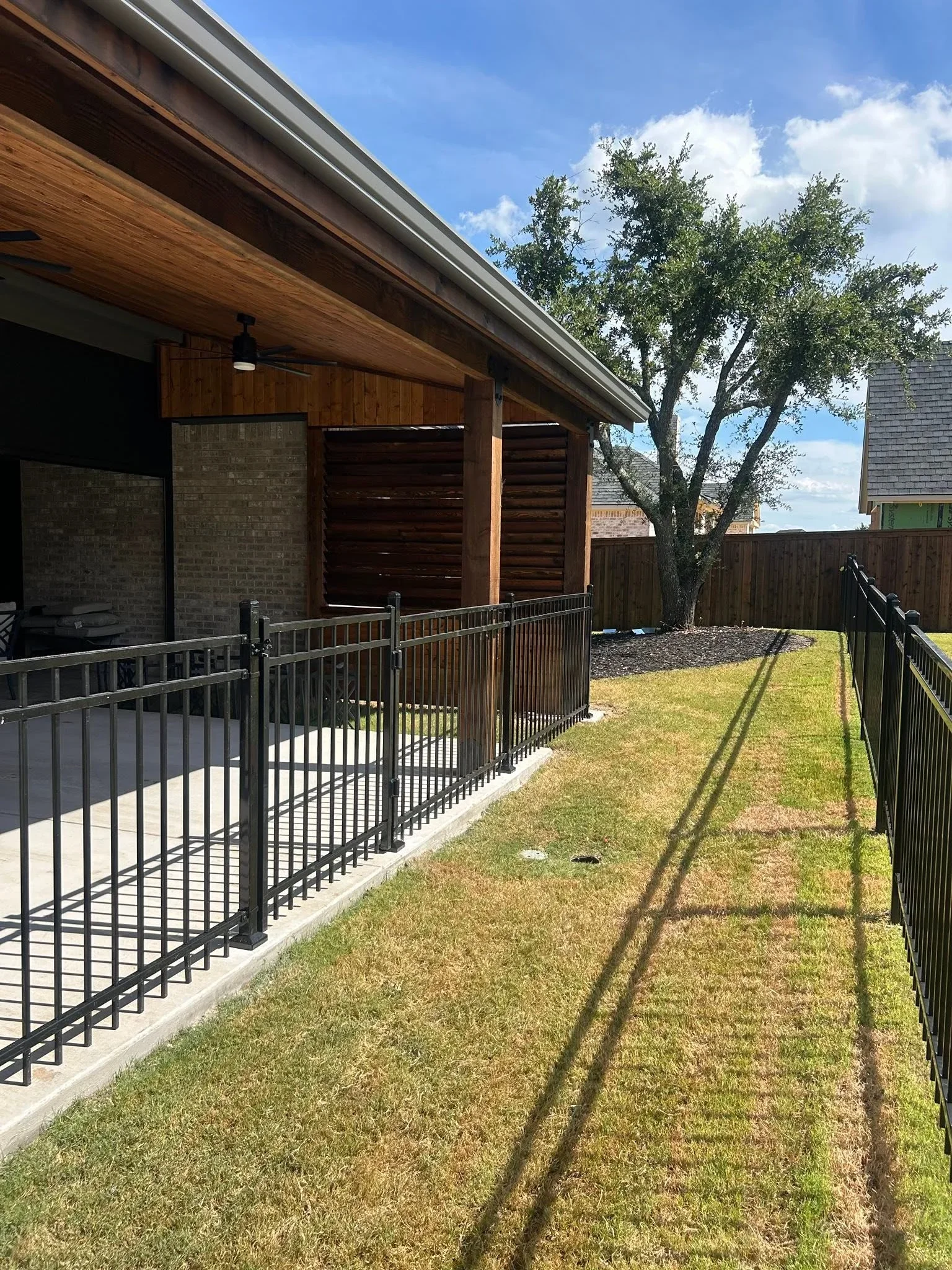 Black metal railing with horizontal slats along concrete patio, wood privacy fence and screens in background