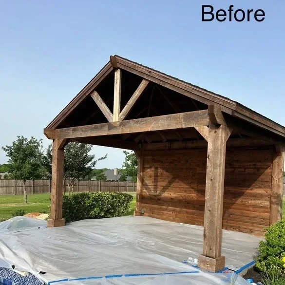 Wooden pavilion with exposed beams, X-bracing, and concrete pad before finishing