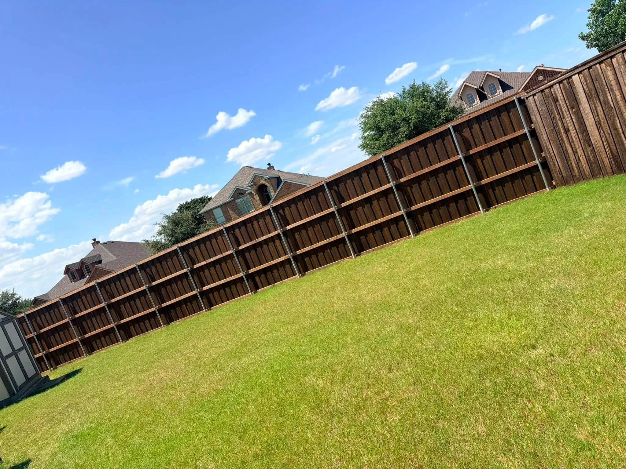 Stained wood privacy fence with vertical boards and copper trim along residential property